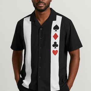 May include: Black button-down shirt with a white vertical stripe down the center and playing card suit symbols. The shirt has short sleeves and a classic collar. The suits are spade, diamond, club, and heart.