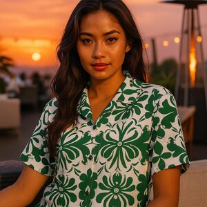 May include: A short-sleeved button-down shirt with a white background and a green floral pattern. The shirt has a classic collar and is worn by a person. The background features a sunset.