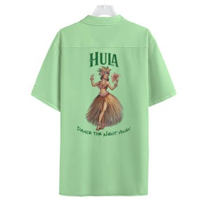 May include: Light green button-up shirt with a Hawaiian theme. The back features a graphic of a woman in a grass skirt with the word "HULA" above and "DANCE THE NIGHT AWAY" below. The shirt has short sleeves and a collar.