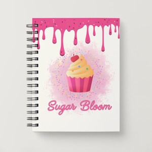 May include: Spiral-bound notebook with a whimsical design. The cover features a cupcake illustration with a cherry on top, surrounded by colorful sprinkles. Pink frosting drips from the top, and the words "Sugar Bloom" are written in cursive.