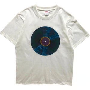 May include: White t-shirt with a graphic of a black vinyl record with a blue and yellow design.