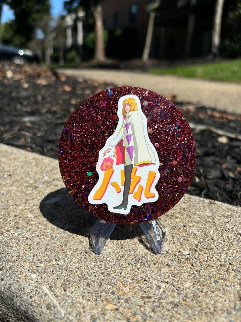 May include: A red glitter round coaster featuring a white anime character wearing a white coat with purple accents and a red and yellow Japanese character in the background.