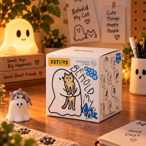 Könnte beinhalten: Eine weiße, quadratische Pappschachtel mit dem Text Behold My Cat und einer Grafik eines Geistes, der eine Katze hält. Die Schachtel zeigt das 52TOYS-Logo und verschiedene Charakterillustrationen. Daneben steht eine kleine Geisterfigur mit einer grauen Katze.