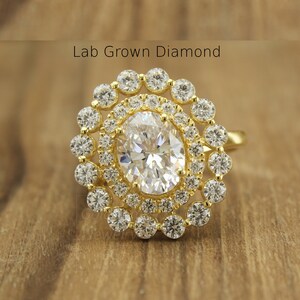 Puede incluir: Un anillo de oro con un gran diamante ovalado cultivado en laboratorio rodeado por un halo de diamantes más pequeños. El anillo tiene un diseño clásico y un aspecto brillante y brillante. El texto "Lab Grown Diamond" es visible.