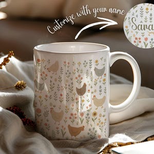 May include: White ceramic mug with a floral pattern featuring chickens and flowers. The mug has a handle and says "Sarah" on the side.
