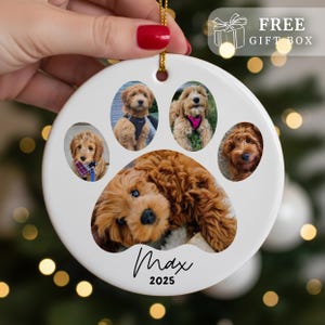 May include: White ceramic paw print ornament with five photos of a dog. The ornament has a gold string for hanging and the text "Max 2025" in a handwritten font. The top right corner has the text "FREE GIFT BOX".