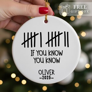 May include: A white ceramic Christmas ornament with a gold string for hanging. The ornament features black tally marks and the text "IF YOU KNOW YOU KNOW" and "OLIVER -2025-". A gift box icon and the words "FREE GIFT BOX" are in the upper right corner.
