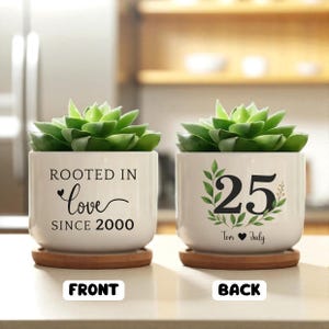 May include: Two white ceramic planters with green succulents. One planter reads "Rooted in Love Since 2000." The other planter displays "25" with "Tom & Judy" below. Both sit on wooden saucers.