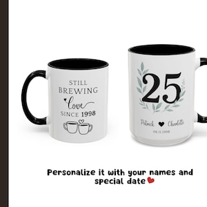 Pu&ograve; includere: Due tazze in ceramica bianca con manici e bordi neri. Una tazza recita "Still Brewing Love Since 1998" con illustrazioni di tazze da caff&egrave;. L'altra tazza mostra il numero "25" con nomi e una data, ideale per un anniversario di matrimonio.