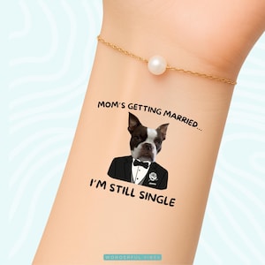 Peut inclure: Tatouage temporaire repr&eacute;sentant un Boston Terrier en smoking avec le texte "Mom's Getting Married... I'm Still Single." Le motif est sur une peau claire, avec un bracelet dor&eacute; et une perle.