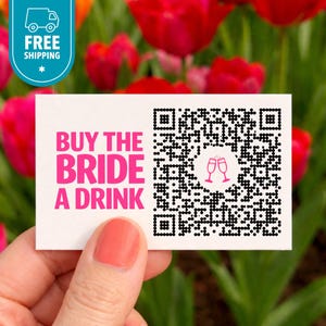 May include: A white card with the text "BUY THE BRIDE A DRINK" in pink, along with a QR code and two pink champagne glasses. The card is held in front of a background of red flowers. A blue and white "FREE SHIPPING" sticker is in the upper left corner.
