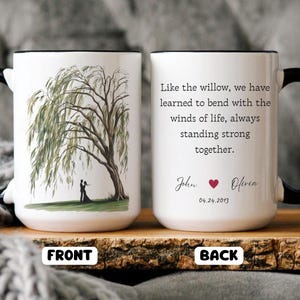 May include: White ceramic mug with a black handle. The front of the mug features a watercolor illustration of a willow tree with a couple standing beneath it. The back of the mug has the text "Like the willow, we have learned to bend with the winds of life, always standing strong together."  The text "John Olivia 04.24.2013" is printed below the quote.