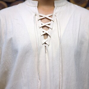 May include: A white linen shirt with a lace-up neckline. The shirt has a relaxed fit and long sleeves.