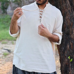 May include: A white linen shirt with a lace-up neckline. The shirt has long sleeves and a relaxed fit.
