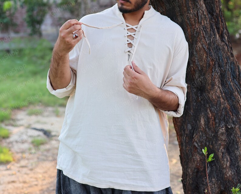 May include: A white linen shirt with a lace-up neckline. The shirt has long sleeves and a relaxed fit.