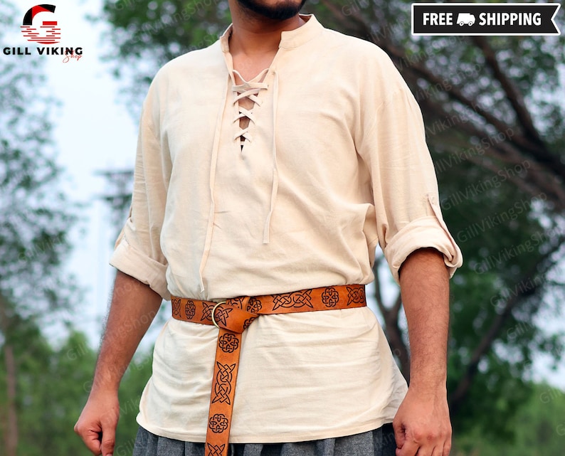 May include: A cream-colored linen shirt with a lace-up neckline and long sleeves. The shirt is worn with a brown leather belt with a Celtic knot design.