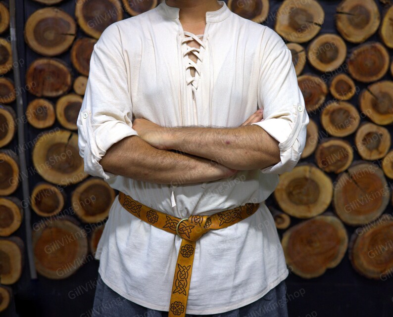May include: A white linen shirt with a lace-up neckline and long sleeves. The shirt is worn with a brown leather belt with a Celtic knot design.
