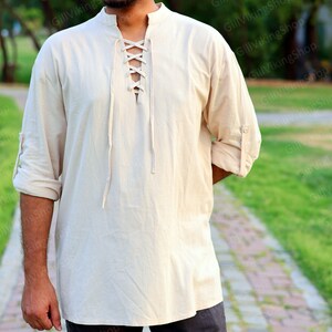 May include: A cream-colored, long-sleeved shirt with a lace-up neckline. The shirt is made of a lightweight fabric and has a relaxed fit.