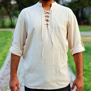 May include: A cream-colored, long-sleeved shirt with a lace-up neckline. The shirt has a relaxed fit and is made of a lightweight fabric.