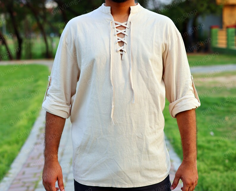 May include: A cream-colored, long-sleeved shirt with a lace-up neckline. The shirt has a relaxed fit and is made of a lightweight fabric.