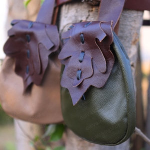 May include: Two leather pouches with brown and green fabric. The pouches have a flap with a decorative design and are attached to a brown leather strap.