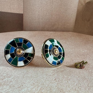 May include: Two cabinet knobs with a gold finish and a circular design. The knobs have a segmented pattern in blue, green, black, and white. Small screws are included. These knobs are suitable for furniture upgrades.