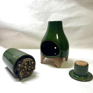 May include: A green ceramic incense burner set, including a cylindrical container, a small lid, and a decorative incense holder. The burner has a distinctive design with a large opening and three small legs. The set is designed for burning incense.