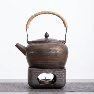 以下が含まれることがあります： ロープの取っ手とウォーマーベースが付いた茶色のセラミックティーポット。 ティーポットには小さな注ぎ口とつまみ付きの蓋が付いています。 ウォーマーベースにはティーライトキャンドルの切り欠きがあります。 ティーポットとウォーマーは灰色の表面にあります。