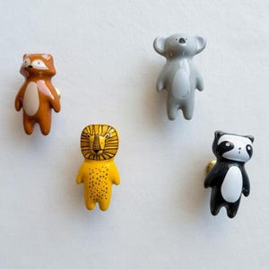 Peut inclure: Quatre boutons de meubles en forme d'animaux. L'ensemble comprend un renard, un koala, un lion et un blaireau, chacun avec des couleurs et des motifs uniques. Les boutons sont probablement en céramique ou dans un matériau similaire, et sont montés avec du matériel doré.