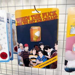 May include: A yellow card with the text "WHEN THE FUCK DID WE GET ICE CREAM?" and a cartoon image of an ice cream cone. The card features a group of cartoon characters, including a man with a red baseball cap and a man with a blue baseball cap.