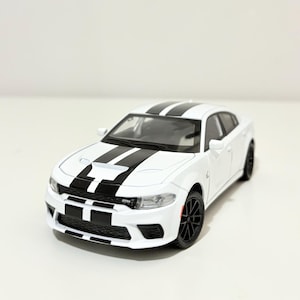 以下が含まれることがあります： 白いモデルカーで、ボンネットと屋根に黒いレーシングストライプが入っています。車は黒いホイールと赤いブレーキキャリパーを備えています。車はセダンタイプです。