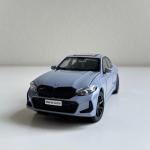 May include: A light gray toy car model of a BMW with a black grill and a license plate that reads "BMW M320i".