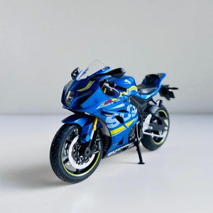 May include: A blue and yellow Suzuki GSX-R1000 motorcycle model. The motorcycle has a black seat and black wheels with yellow accents.