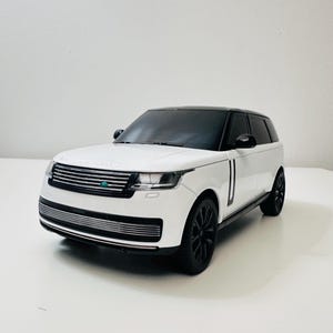 Puede incluir: Un SUV blanco con techo negro y ruedas negras. La parrilla delantera es negra con un borde plateado. El coche tiene un diseño elegante y moderno y está sobre una superficie blanca.