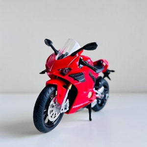 May include: A red and black toy motorcycle with a clear windshield. The motorcycle is a replica of a sport bike.