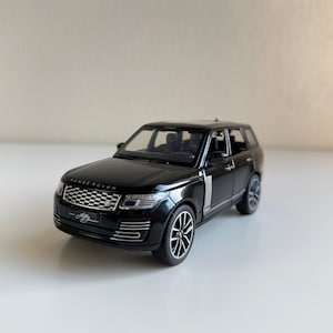 Puede incluir: Modelo de coche de juguete negro de un Range Rover con una parrilla plateada y detalles plateados. El coche tiene un interior negro y las palabras "Range Rover" son visibles en la parte delantera del coche.