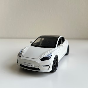 May include: White toy car model of a Tesla Model 3.