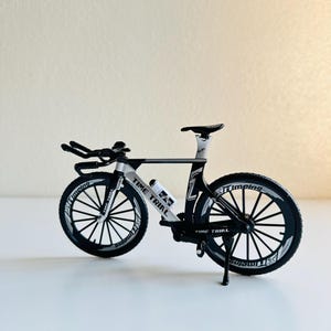 May include: A black and white time trial bicycle with a white water bottle holder and the words "Time Trial" printed on the frame.