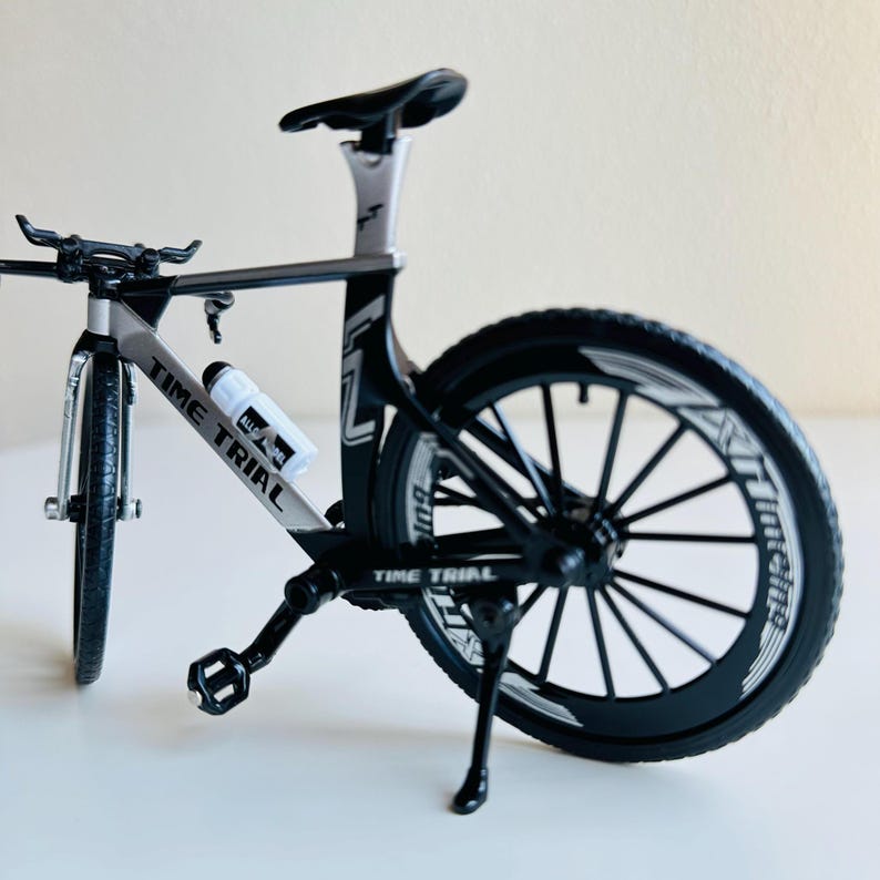 May include: A black and silver Time Trial bicycle with a water bottle holder. The bicycle has a black kickstand and black wheels with white lettering.