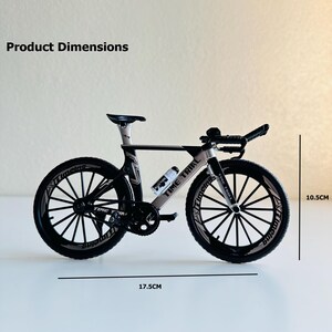 May include: Black and white toy bicycle model with the words "Time Trial" printed on the frame. The bicycle is 17.5 inches long and 10.5 inches tall.