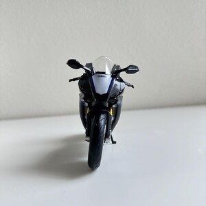 May include: A black, white, and blue Yamaha R1 model motorcycle. The model has a clear windshield, black side mirrors, and the Yamaha logo is visible. The motorcycle is a detailed replica of a sport bike.