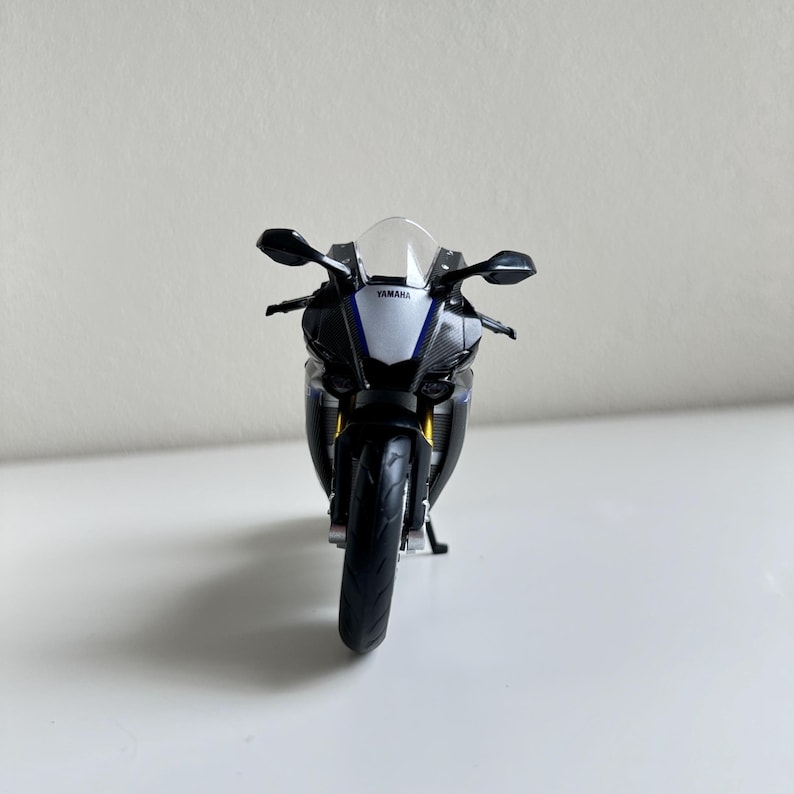 May include: A black, white, and blue Yamaha R1 model motorcycle. The model has a clear windshield, black side mirrors, and the Yamaha logo is visible. The motorcycle is a detailed replica of a sport bike.