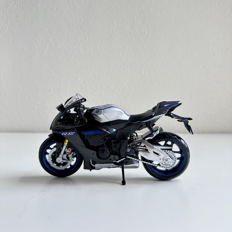 May include: A detailed model motorcycle in black, silver, and blue. The miniature bike features realistic details, including wheels, a seat, and a windshield. The model has the letters "RM" on the side.