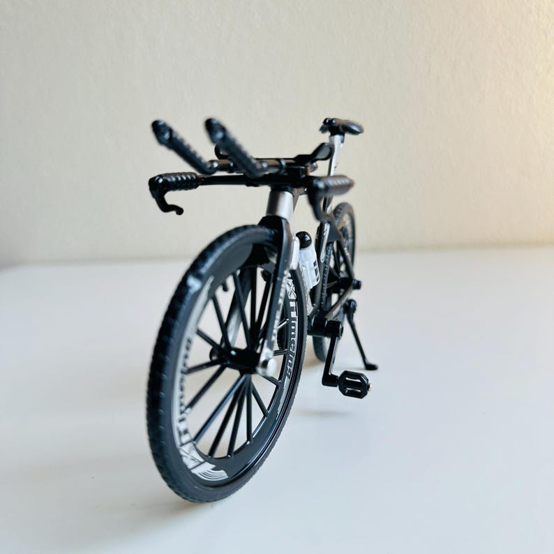 May include: A black toy bicycle with a silver frame and black wheels. The bicycle has a kickstand and a handlebar with two sets of handlebars.