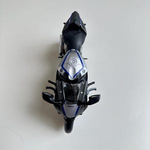 May include: A top-down view of a Yamaha motorcycle model. The motorcycle is primarily black, silver, and blue. The Yamaha logo is visible on the front. The model has detailed features, including mirrors and a windshield.