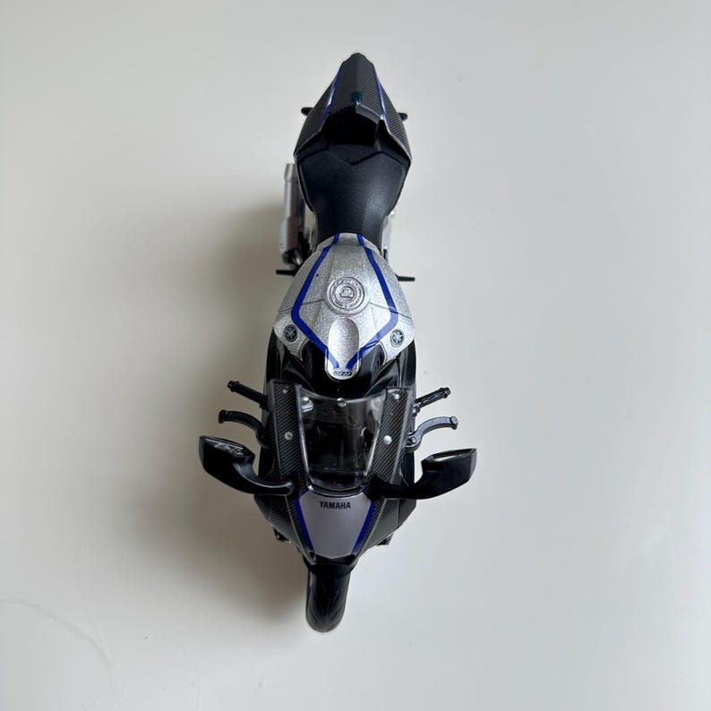May include: A top-down view of a Yamaha motorcycle model. The motorcycle is primarily black, silver, and blue. The Yamaha logo is visible on the front. The model has detailed features, including mirrors and a windshield.