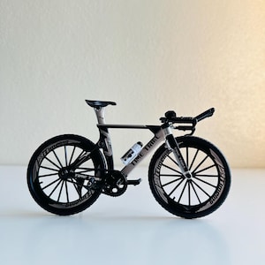 May include: A black and silver time trial bicycle model with black wheels and white lettering that says "Time Trial" on the frame.