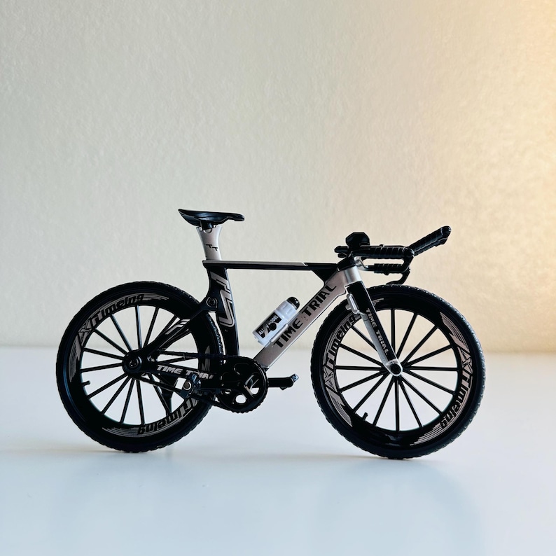 May include: A black and silver time trial bicycle model with black wheels and white lettering that says "Time Trial" on the frame.