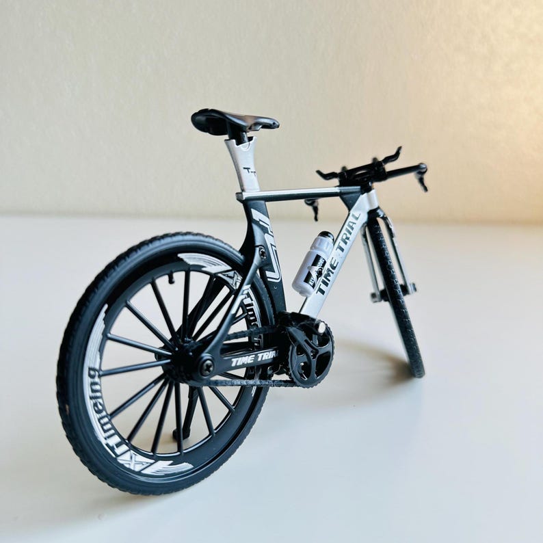 May include: A black and white time trial bicycle with a water bottle holder. The bicycle has a black frame, black wheels, and white accents. The water bottle holder is on the frame and says "Time Trial".