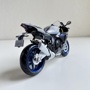 May include: A detailed model of a Yamaha R1 motorcycle. The bike features a black, silver, and blue color scheme with a visible exhaust pipe and blue rims. The license plate reads "YAMAHA".
